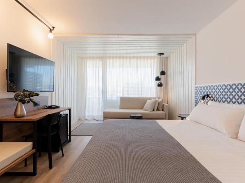 Modern hotelkamer met groot bed, tv, bureau en zithoek met bank.