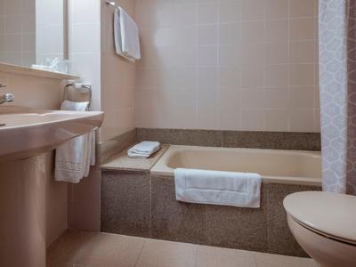 Bagno moderno con vasca, lavabo e asciugamani in tonalità neutre.