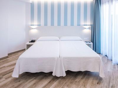 Due letti singoli bianchi in una stanza d'hotel luminosa con parete a righe blu e pavimento in legno.