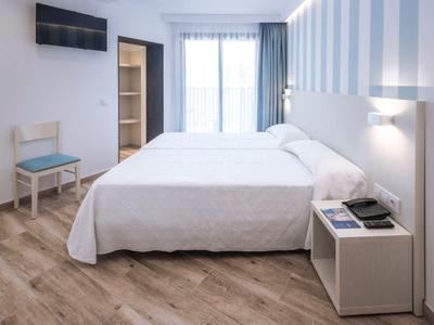 Camera d'hotel arredata semplicemente con letto matrimoniale, finestra e mobili in legno chiaro.