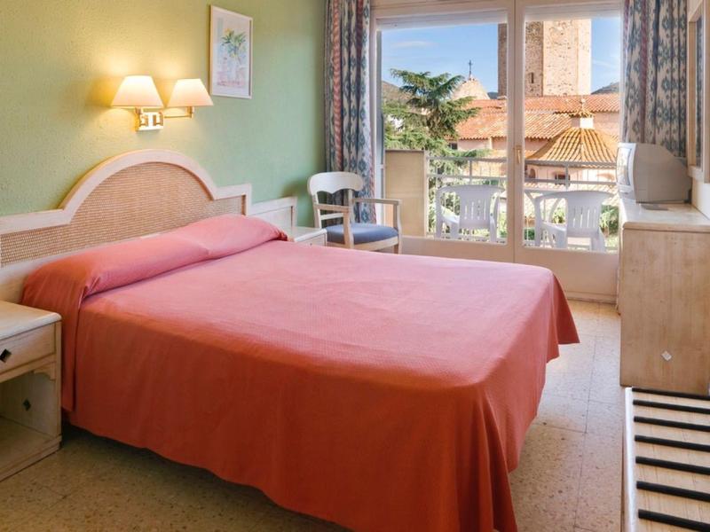 Camera d'hotel luminosa arredata con letto matrimoniale e vista su un albero fuori dalla finestra.