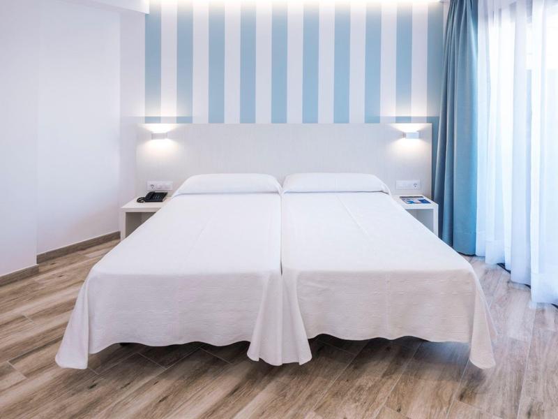 Due letti singoli bianchi in una stanza d'hotel luminosa con parete a righe blu e pavimento in legno.