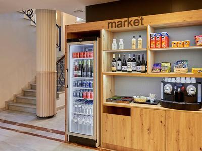 Un petit marché d'hôtel avec réfrigérateur, étagères et machine à café dans une zone d'entrée.