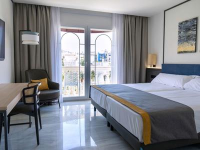 Chambre d'hôtel moderne avec grand lit, bureau et balcon avec vue sur l'extérieur.