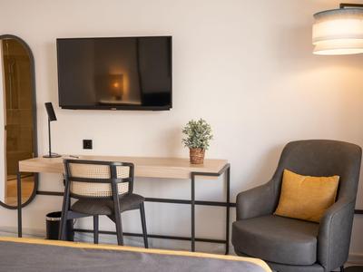 Espace chambre d'hôtel moderne avec bureau, chaise, fauteuil et télévision murale.