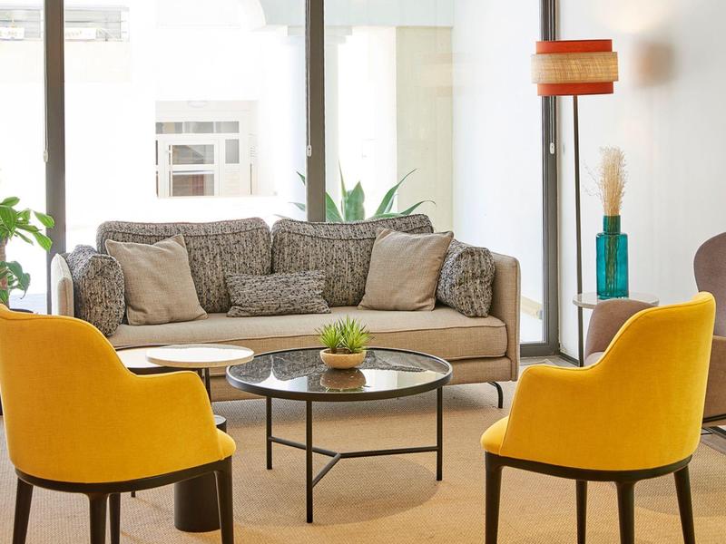 Modern ingerichte woonkamer met grijze bank en twee gele fauteuils voor grote ramen.