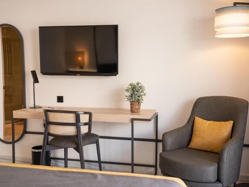 Gezellige hotelkamerhoek met stoel, bureau, tv, spiegel en leeslamp.