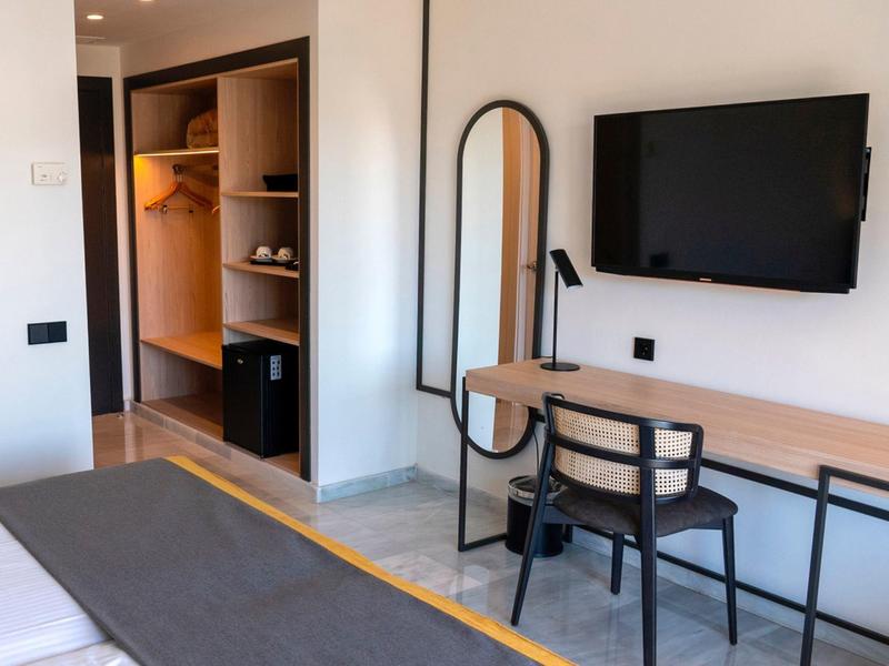 Moderne hotelkamer met bureau, stoel, wandspiegel en open kledingkast.