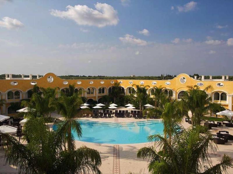 Großer Pool in der Mitte mit Palmen und gelben Gebäuden unter blauem Himmel.