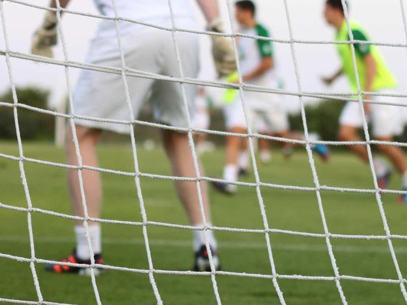 Fußbälle vor dem Tor, dahinter Torwart und Spieler auf grünem Spielfeld.