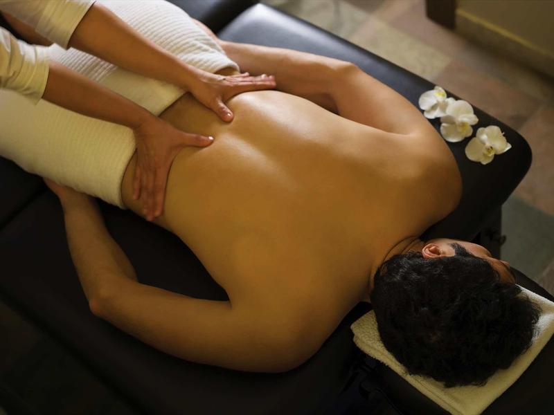 Person liegt mit nacktem Rücken auf Massagetisch, Hände massieren die Schultern, ruhige Atmosphäre.