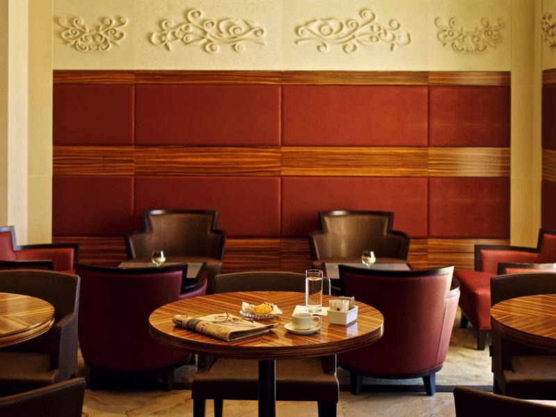 Gemütlicher Cafébereich mit runden Holztischen, bequemen Ledersesseln und dekorativen Wandpanelen.