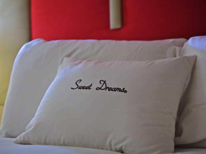 Kissen mit Schriftzug "Sweet Dreams" vor roten und weißen Kopfkissen auf einem Bett.