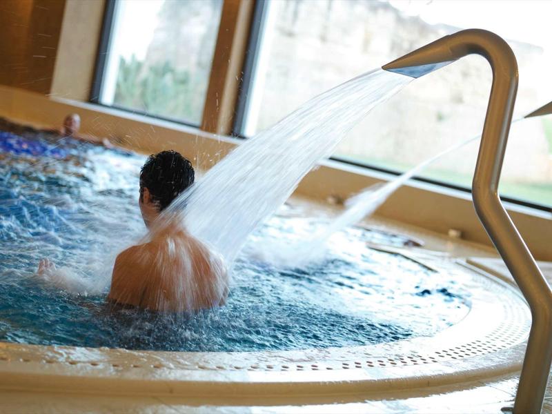 Mann entspannt in einem Whirlpool mit Wasserstrahl in einem hellen Innenraum.