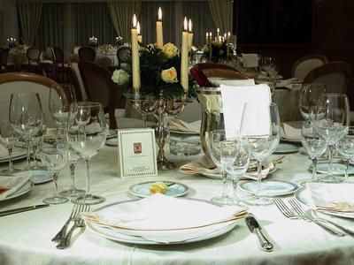 Eleganter runder Tisch mit weißer Tischdecke, Kerzen, Blumen und eingedecktem Geschirr im Restaurant.