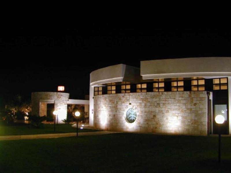 Modernes Gebäude aus hellem Stein, beleuchtet bei Nacht mit runden Lampen und dunklem Nachthimmel.