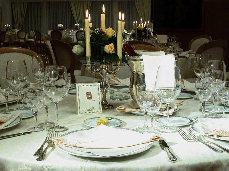 Eleganter runder Tisch mit weißer Tischdecke, Kerzen, Blumen und eingedecktem Geschirr im Restaurant.