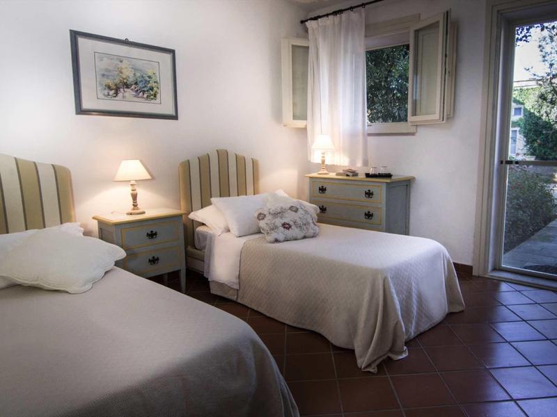 Schlichtes Schlafzimmer mit zwei Einzelbetten, Nachttisch, Lampe, Fenster und geöffneter Tür zum Garten.