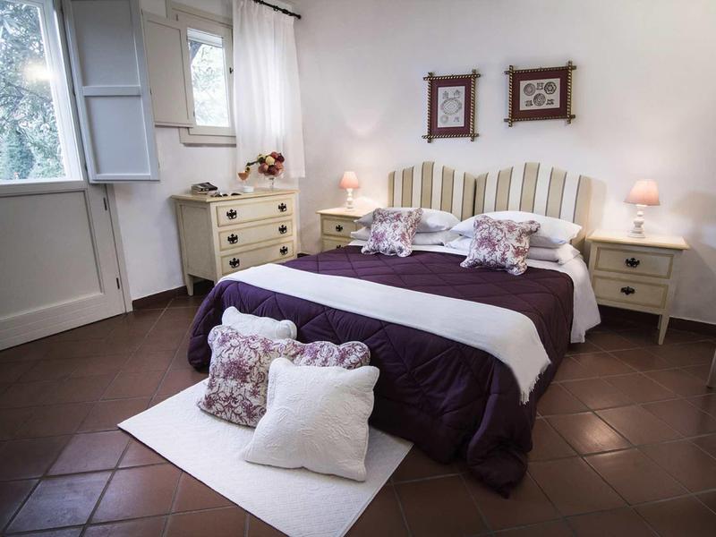 Gemütliches Schlafzimmer mit Doppelbett, weißen Möbeln und lila Bettdecke, zwei Fenstern und Deko.