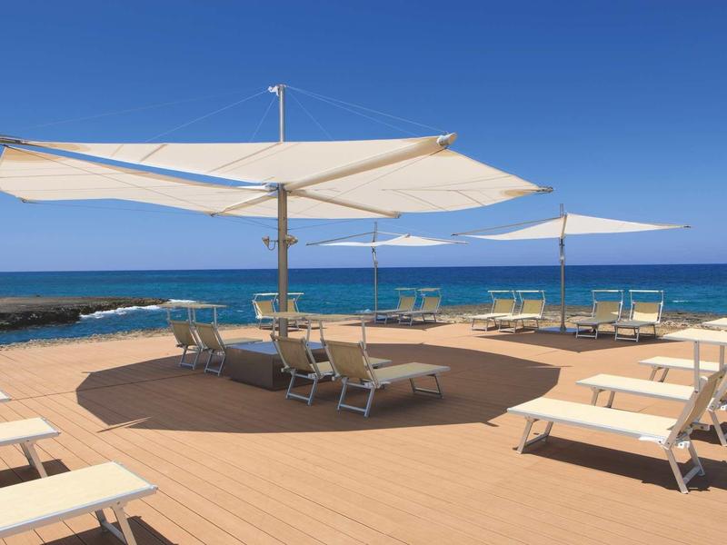 Terraza con tumbonas y grandes sombrillas con vista al mar en un día soleado.