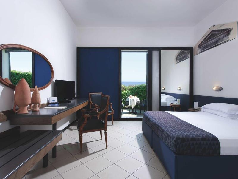 Habitación de hotel moderna con cama doble, escritorio, silla y balcón con vista.