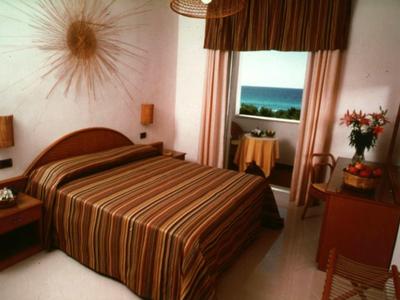 Gemütliches Schlafzimmer mit gestreiftem Bett, Holzmöbeln und Meerblick durch das Fenster.