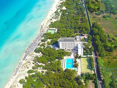 Luftaufnahme eines Strandes mit türkisfarbenem Wasser, Hotelanlage, Pool und grüner Vegetation.