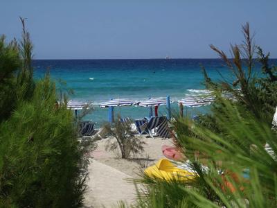 Blick durch grüne Pflanzen auf Strandliegen und Sonnenschirme am türkisblauen Meer