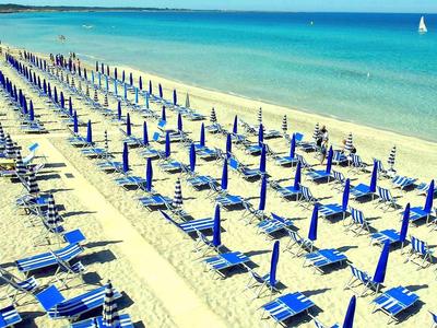 Leerer Strand mit blauen Sonnenschirmen und Liegestühlen, Meer im Hintergrund.