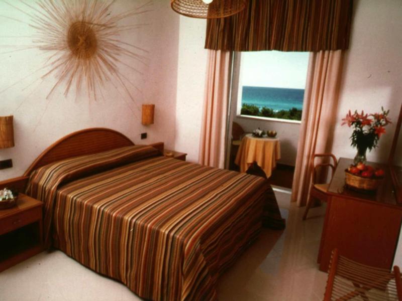 Gemütliches Schlafzimmer mit gestreiftem Bett, Holzmöbeln und Meerblick durch das Fenster.