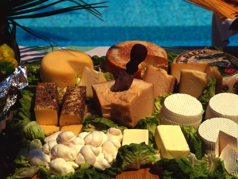 Verschiedene Käsesorten in runder und eckiger Form, umgeben von grünem Salat auf Holzbrett.