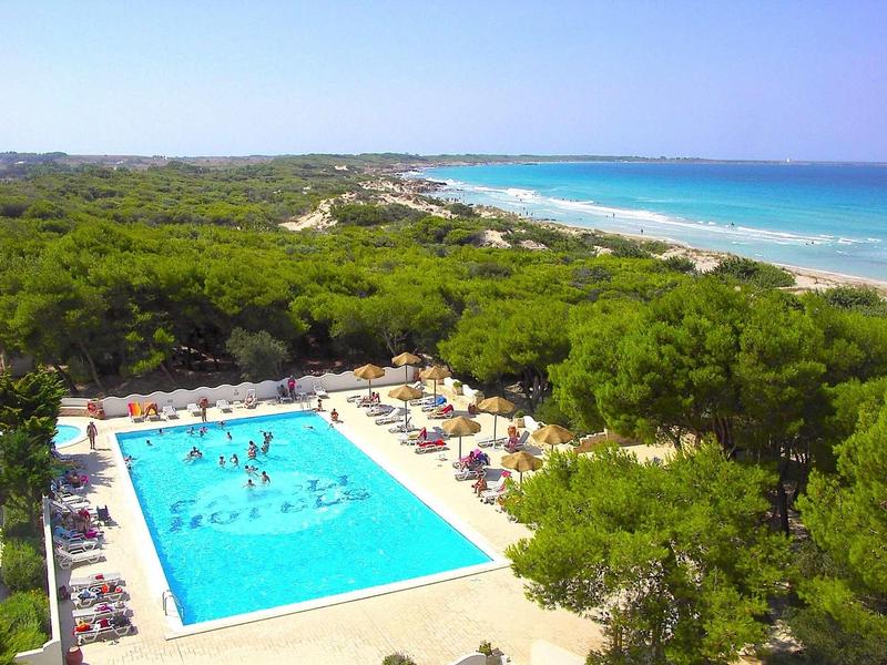 Schwimmbad mit Menschen, umgeben von grünen Bäumen und Blick auf das blaue Meer im Hintergrund.
