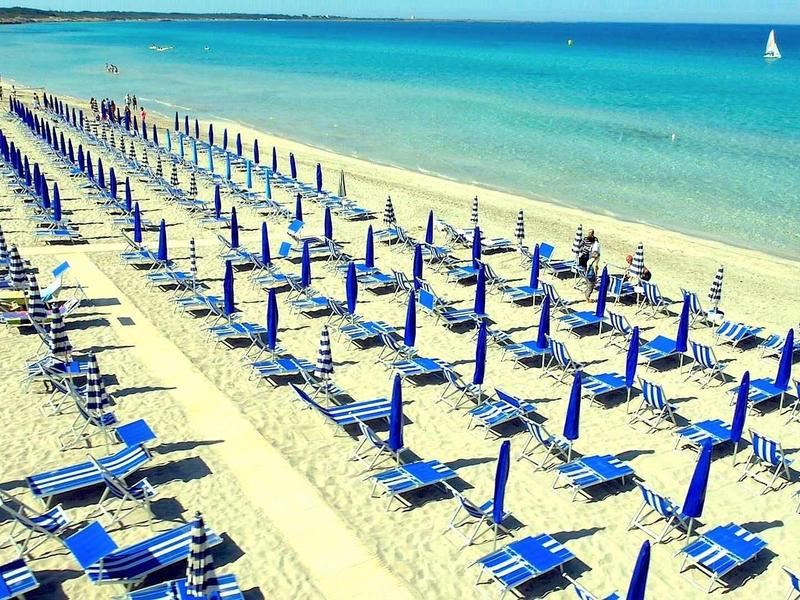 Leerer Sandstrand mit vielen blauen Liegestühlen und geschlossenen Sonnenschirmen am Meer.