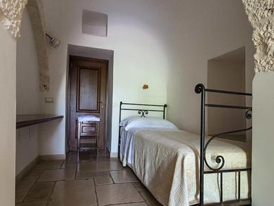 Blick durch einen gewölbten Eingang auf ein einfaches Schlafzimmer mit Eisenbett und Holztür.