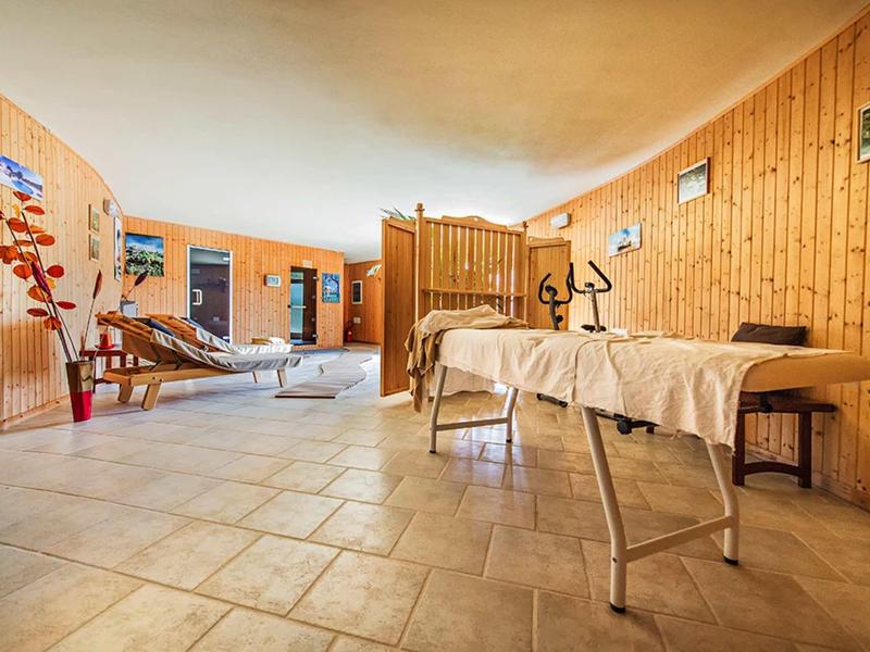 Licht ingerichte wellnessruimte met massagetafels, relaxstoelen, houten wanden en tegelvloer.