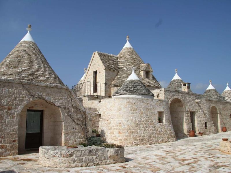 Traditionele trulli-huizen met kegelvormige daken en licht steen onder een zonnige hemel.