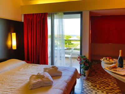 Gemütliches Hotelzimmer mit Doppelbett, roter Gardine und Balkon mit Ausblick.