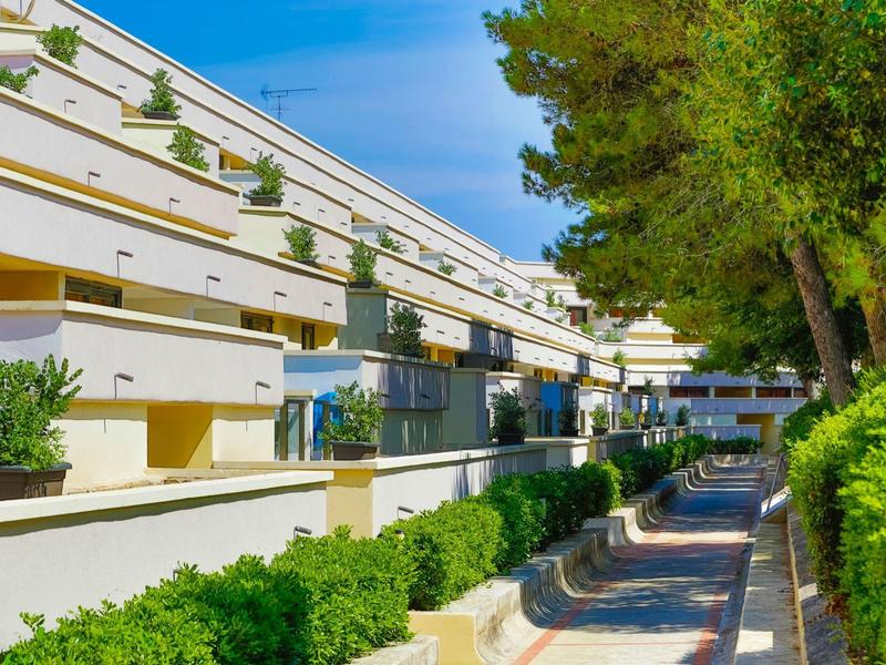 Complexe hôtelier moderne avec balcons, plantes et allée extérieure ensoleillée.