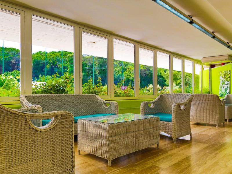 Salon lumineux avec mobilier en osier et grandes fenêtres donnant sur la verdure.