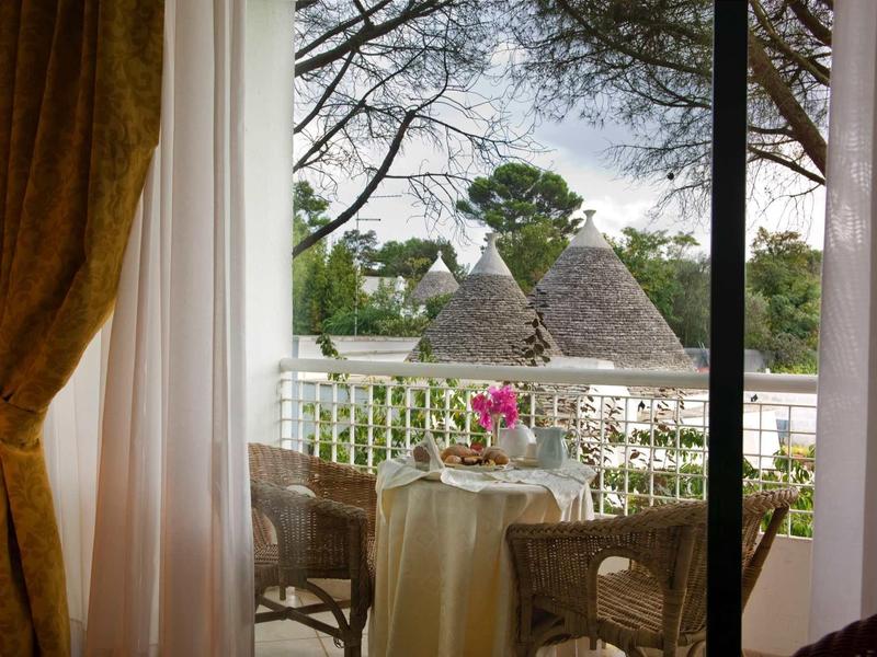 Blick durch Fenster auf Terrasse mit Tisch, zwei Stühlen und exotischer Gartenlandschaft.