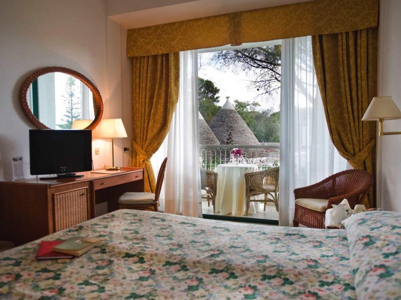 Gemütliches Schlafzimmer mit Blumenbettwäsche, Schreibtisch, Fernseher und Balkon mit Blick ins Grüne.