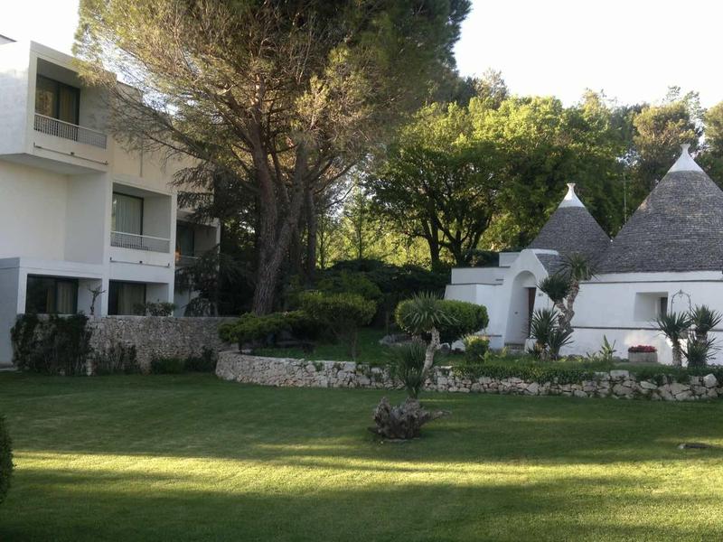 Grünes Garten mit gepflegtem Rasen, Bäumen und einem weißen Gebäude mit kegelförmigen Dächern.