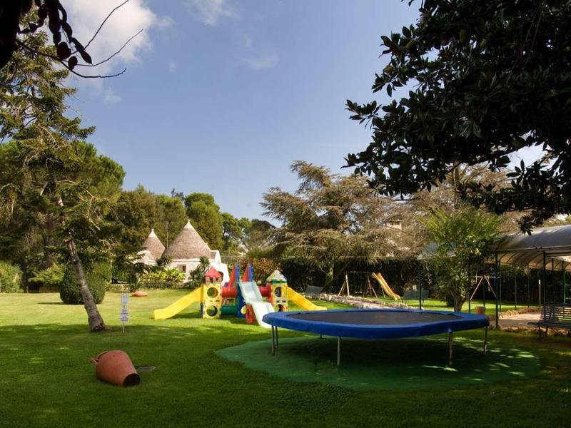 Garten mit Rasen, Trampolin, Spielturm, Kind und Bäumen bei sonnigem Himmel.