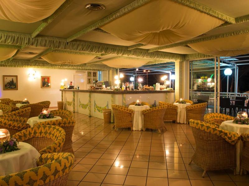 Gemütliche Bar mit gelben Sesseln, Tischen, Kachelboden und großer Fensterfront bei Nacht.