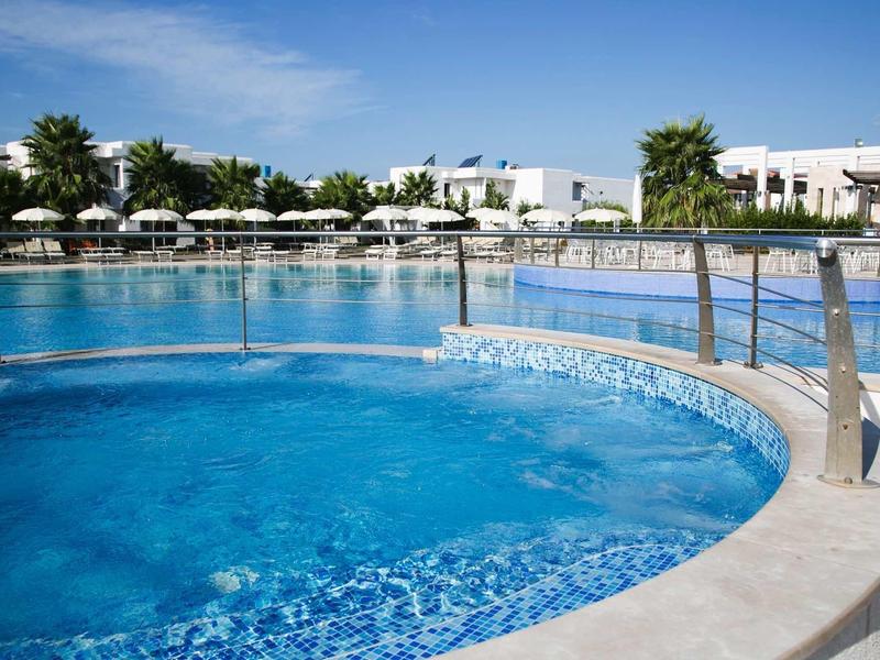 Round pool with clear water and hotel buildings in the background on a sunny day.