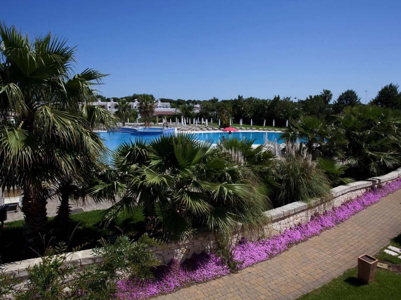 Pool with blooming flowers and palm trees in a holiday resort under clear sky.