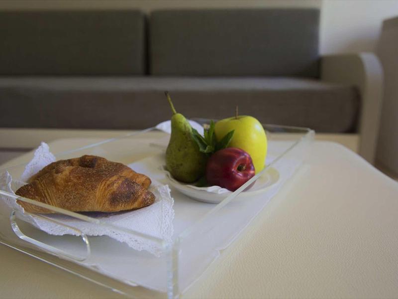 Breakfast with croissant, apple, and grape on a white table in front of a grey sofa.