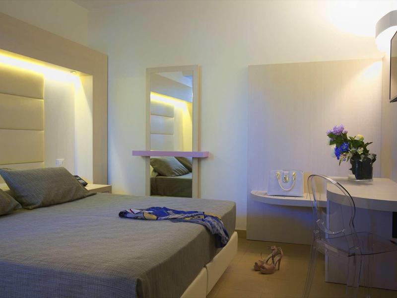 Modern hotel room with double bed, desk, chair, and geranium on the table.