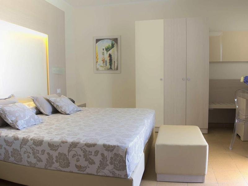 Bright hotel room with large bed, comfortable pillows, and a white wardrobe.