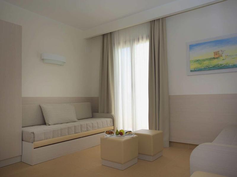 Bright hotel room with sofa, two stools, curtains, and a wall painting.